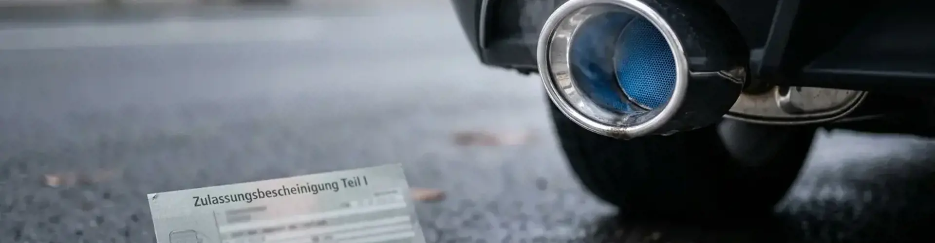 Detail-Aufnahme Auspuff eines Diesel-Pkw mit Fahrzeugschein im Vordergrund - Symbolbild Euro-Norm und Schadstoffklasse