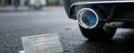Detail-Aufnahme Auspuff eines Diesel-Pkw mit Fahrzeugschein im Vordergrund - Symbolbild Euro-Norm und Schadstoffklasse
