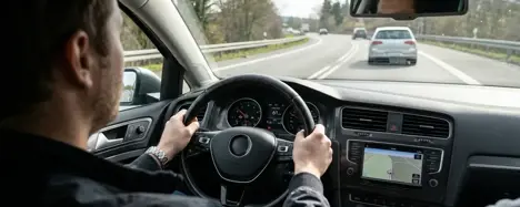 Konzentrierter Fahrer im Cockpit eines Gebrauchtwagens während einer Probefahrt, Hände am Lenkrad, Blick auf die Straße